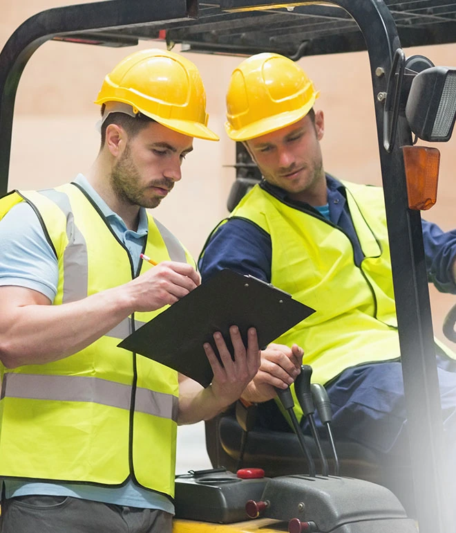 Warehouse associates reviewing a checklist beside a forklift